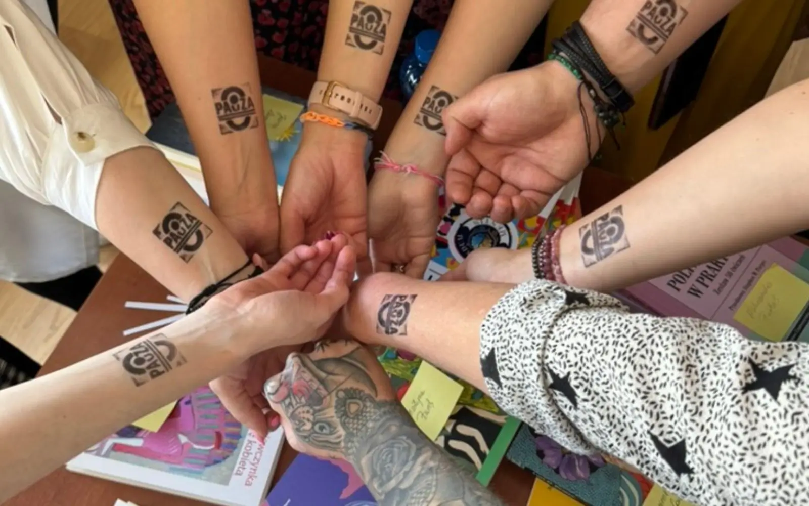 ręce złączone w kole, na przedramionach pieczątki z napisem "PAUZA"