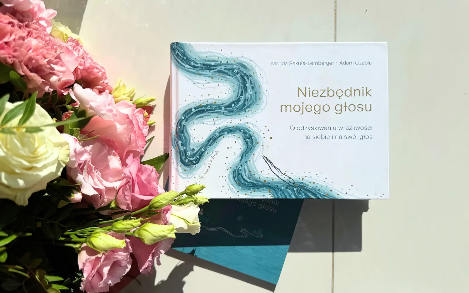 książka "niezbędnik mojego głosu", obok bukiet kwiatów